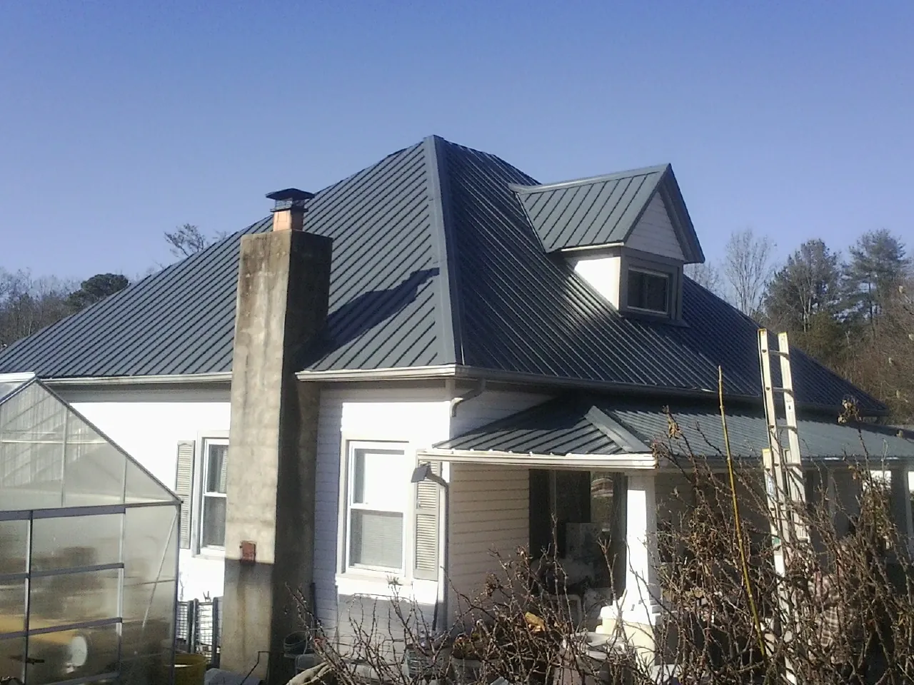 Dark blue standing seam metal roof on a white farmhouse with dormer — Slate & Tile Roof Repair by Roofing Brothers in Moline