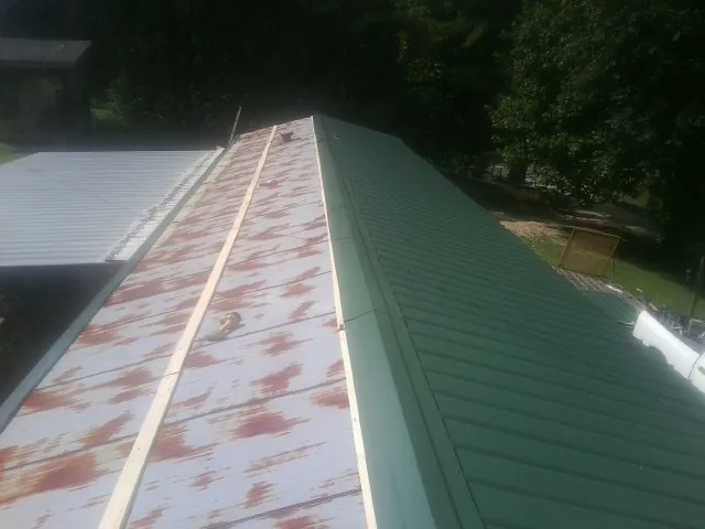Old rusted panels beside newly installed green metal roofing — Wind Damage Roof Repair by Roofing Brothers in Moline