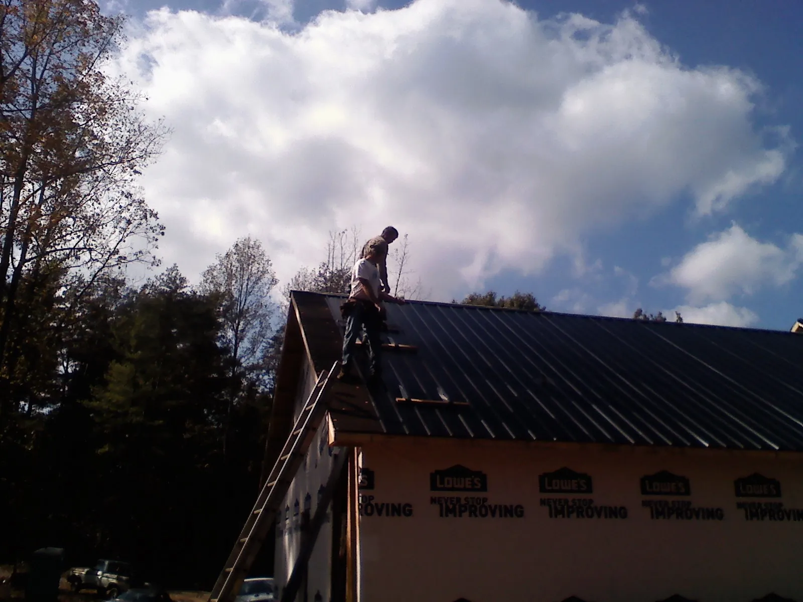 Roofer fastening dark metal panels high against a cloudy sky, from a Roof Inspection job in Moline