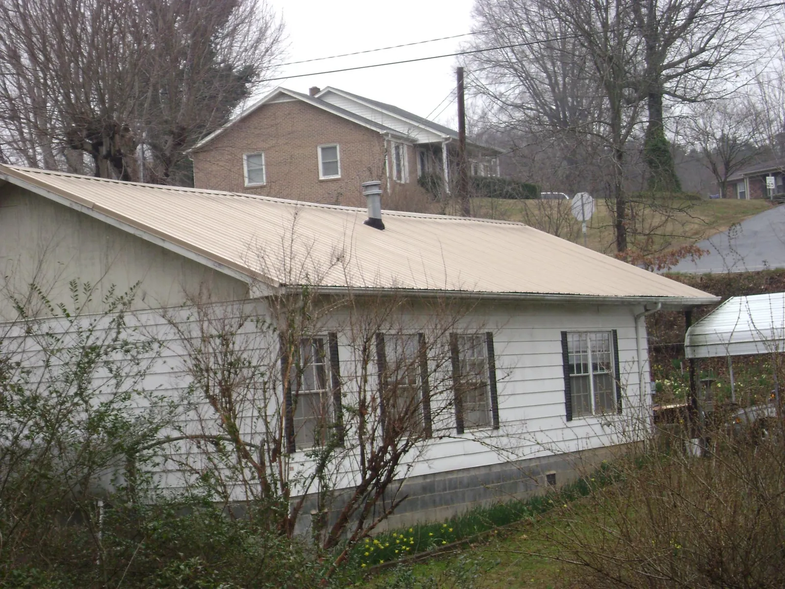 Tan metal roof on a white sided house set into a hillside — Commercial Roofing by Roofing Brothers in Moline